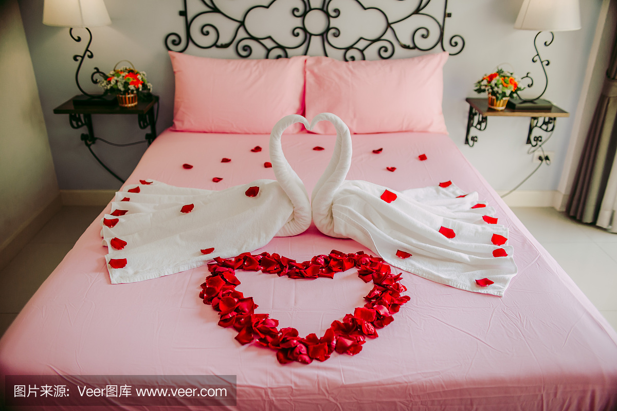 豪华酒店的床上装饰着玫瑰花瓣和双白天鹅形状的织物。